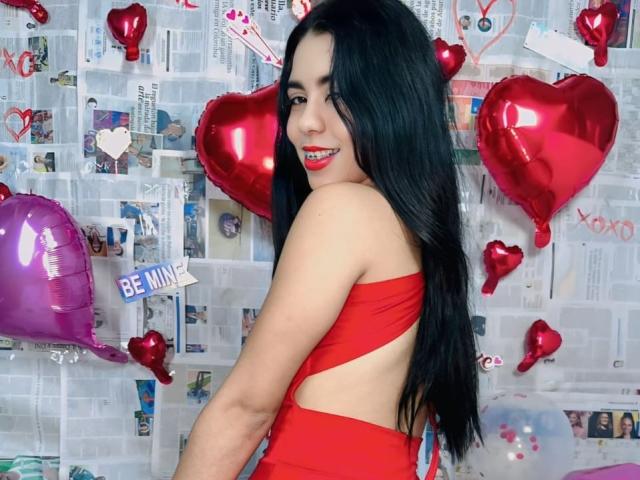 InocentLooks with long black hair, red cutout dress, smiling at camera, red and purple heart balloons, looking over shoulder, showing her ass, cute and sexy, red lipstick.