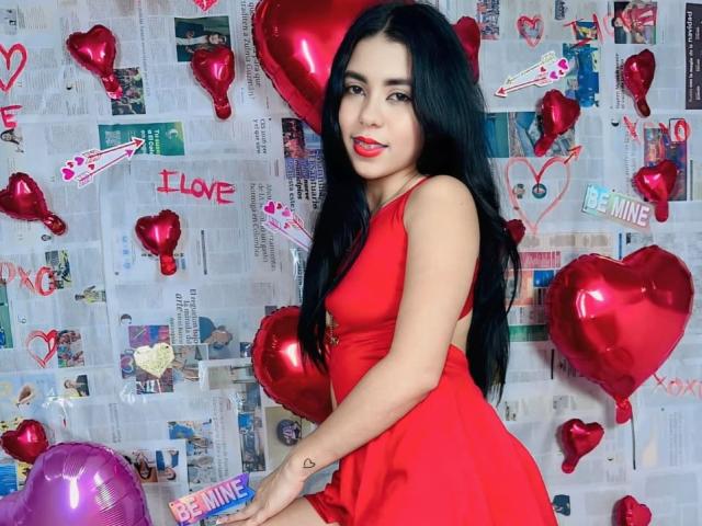 InocentLooks with long black hair, red dress, red lipstick, and red heart balloons, showing her ass, smiling, standing, holding pink balloon, newspaper background.