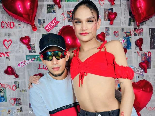 UnitedSou, con los pechos pequeños, una camiseta roja ajustada y el abdomen descubierto, está de pie junto a UnitedSou, que lleva un sombrero y gafas de sol, rodeados de globos con forma de corazón rojos. La mano de UnitedSou está sobre la espalda de UnitedSou..