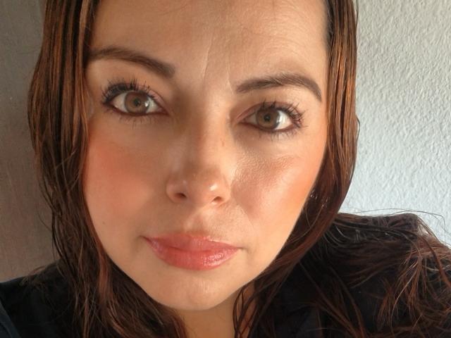 Seher's face, brown eyes, slightly wavy brown hair, light skin, subtle makeup, pinkish lips, and a neutral expression, looking directly at the camera.
