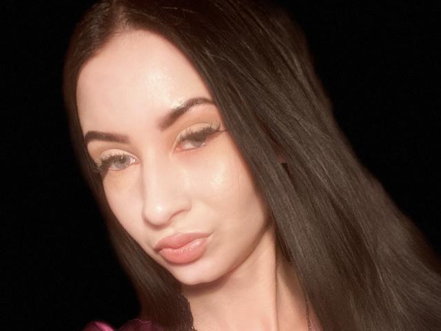 StarrySiren has long, straight black hair, light skin, and full pink lips. She's winking with her right eye, showing off her long, dark eyelashes. Her nose is small.