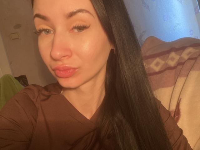 StarrySiren has shiny skin, pink pout, and long black hair, wearing a brown shirt, with a slight pout, and soft, warm lighting.