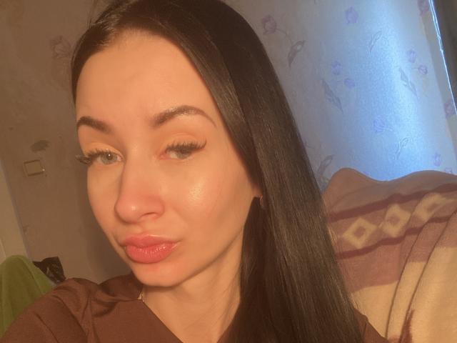 StarrySiren has glossy pink lips, long black hair, and thick eyelashes. Her light skin is slightly shiny, and she's looking down with a slight pout.