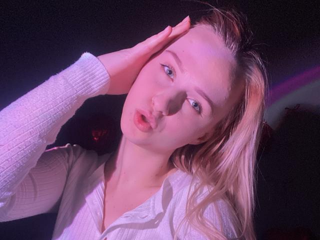 FlyFreedom with pouty pink lips, blonde hair, white ribbed shirt, hand on head, pinkish-purple lighting, blue eyes, looking slightly up, soft pinkish glow on skin, medium tits.