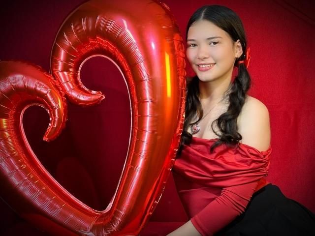 LizzieSweets with red heart balloons, wearing off-shoulder red top, black skirt, smiling, long black pigtails, red earrings, red background, shiny metallic balloons, cute, sexy.