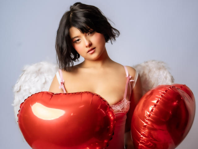MisakiWong with short black hair, wearing pink lingerie and white feather wings, holding shiny red heart balloons, showing small tits and a cute face, looking slightly down.