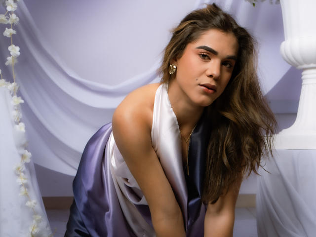 AliceCoolenk with long brown hair, wearing a shiny purple and white satin dress, leaning forward, showing her small tits, with a slightly open mouth and a seductive look.