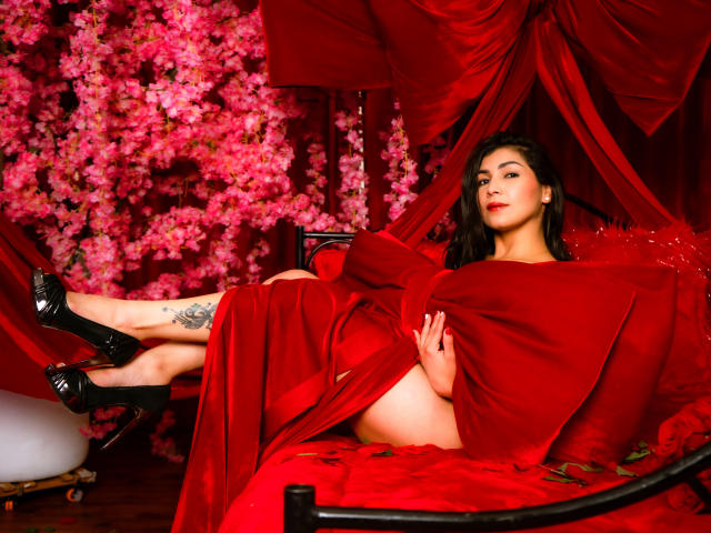 ChanelBrouw with red dress, black heels, tattoo on thigh, legs up, red curtain, pink flowers, sitting on red pillow, looking at camera, sexy, confident, red background.