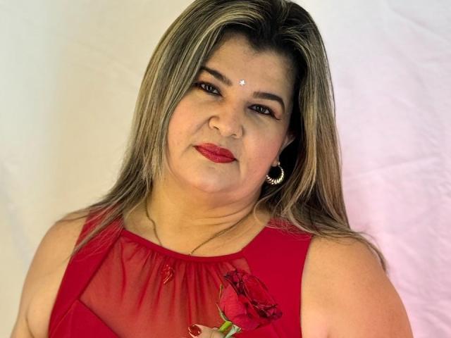 AdrianaPrettie with red lipstick, medium tits, red sheer dress, rose, blonde highlights, brown eyes, nose ring, earring, white background, soft smile, slightly chubby, medium-length hair.