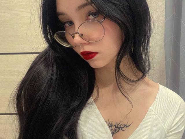 Yasumiu with long black hair, red lipstick, glasses, nose ring, white top, and tribal tattoo on chest. Her tits are small, and she has a sexy, cute look.