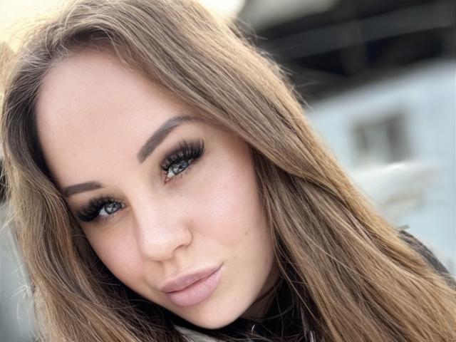 Ariya69's face, showing off her long brown hair, big green eyes with heavy eyelashes, and pink lips. She's making a slight pouty expression, looking cute and sexy.