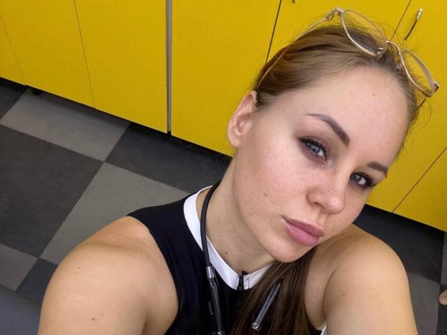 Ariya69, with brown hair and glasses on her head, has pouty lips, black tank top, and a lanyard, showing off her tits in a selfie.