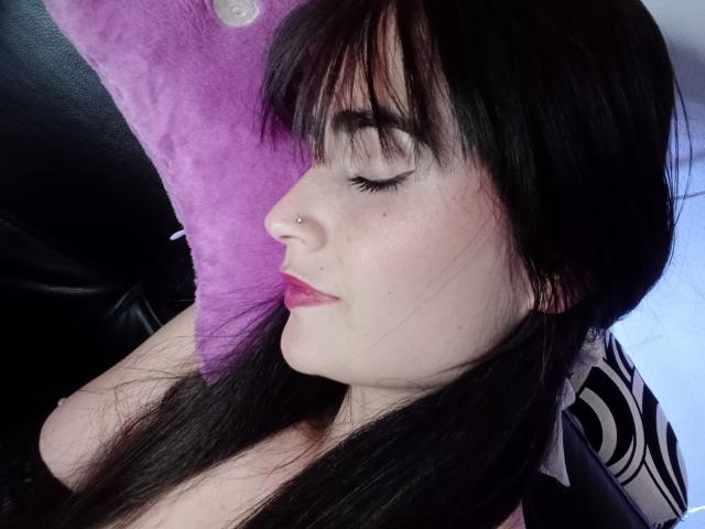 EllieBonneth has pale skin, black hair, and a nose piercing. She's sleeping with pink lips, closed eyes, and a purple pillow. Boobs are not visible.