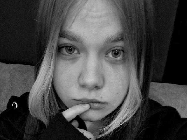 Black-and-white selfie of Lerinda with blonde hair, pensive expression, finger slightly touching her bottom lip, wearing a dark hoodie, showcasing her small, round nose and slightly upturned eyes.