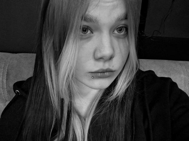 Lerinda has long, straight, blonde hair, a lip piercing, and a small beauty mark on her chin. She's wearing a dark hoodie, looking serious in a black-and-white photo.