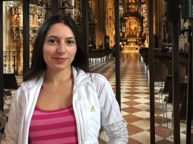 JainFresh-hot with medium tits, pink striped shirt, white Adidas jacket, dark hair, smiling, standing in a church with checkered floor, wooden chairs, and ornate altar in background.