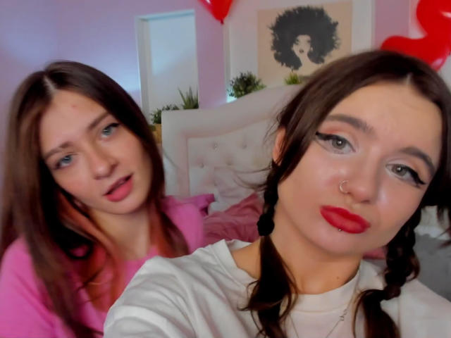 MaoandLulu with brown hair, red lipstick, and nose ring, wearing white shirt, in front of MaoandLulu with pink shirt, brown hair, and open mouth. Both have sexy faces.