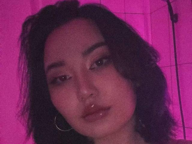 KitsuneKayo has dark curly hair, a nose ring, hoop earrings, and shiny lips, with pink-tinted skin and half-closed eyes, looking slightly bored or indifferent.