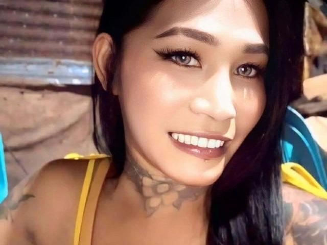 MisstessGalaxia-hot has a tattoo on her neck, black hair, and a smile showing her white teeth. She's wearing a yellow top with a blue strap.