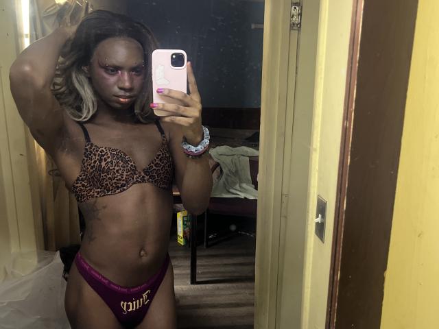 HaitianPearl with dark skin, wearing a leopard print bra and purple "yami" panties, holding a pink phone, arm raised, mirror selfie, blonde hair, pink eye makeup, pink nails.
