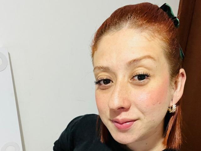 Valeriaaf has red hair in a green clip, light skin, and is smiling with her lips slightly puckered. She's wearing black and has long eyelashes with small earrings.