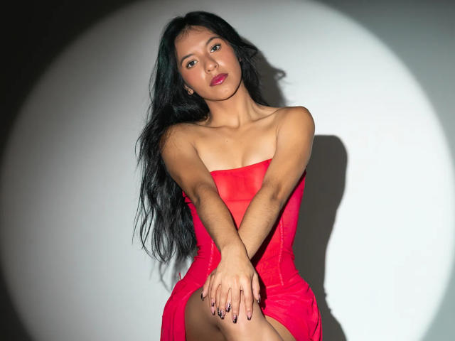 AlissaCavalli with long black hair, wearing a strapless red dress, sitting with hands on knees, looking at camera, slightly parted lips, soft shadow, light skin, Asian, sexy.