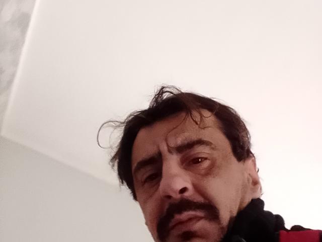 Dragone69 has messy dark hair, a thick mustache, and a slightly annoyed expression. His face is tilted downward, showing a red shirt's collar in the lower right.