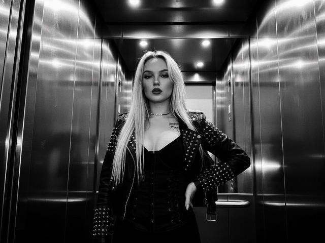 JaneOSweetAh with long blonde hair, dark lipstick, black studded jacket, black corset, standing in a metallic elevator, hand on hip, looking confident, black and white, high contrast.