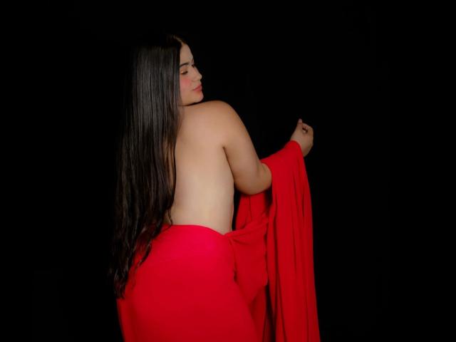 MiahKumarI with long black hair, topless, holding a red cloth over her ass and tits, facing away, dark background, soft lighting, confident pose.