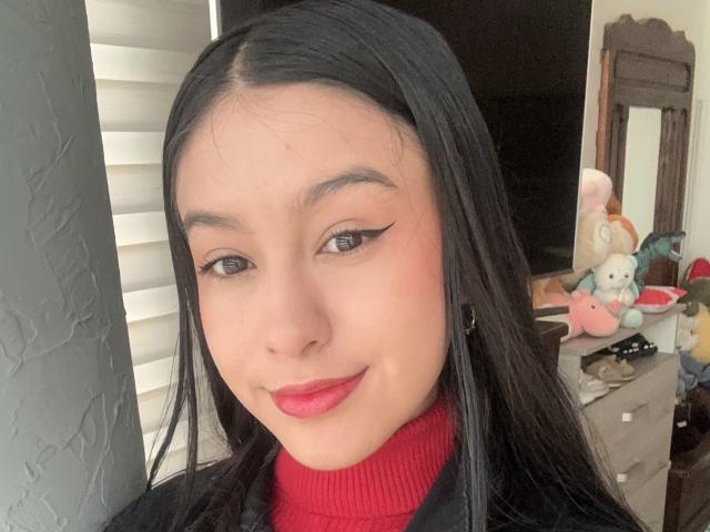 Soranaa a de longs cheveux noirs, du rouge à lèvres, et du crayon pour les yeux, elle porte un pull rouge à col roulé, avec un joli sourire et un petit nez. Ses fesses ne sont pas visibles..