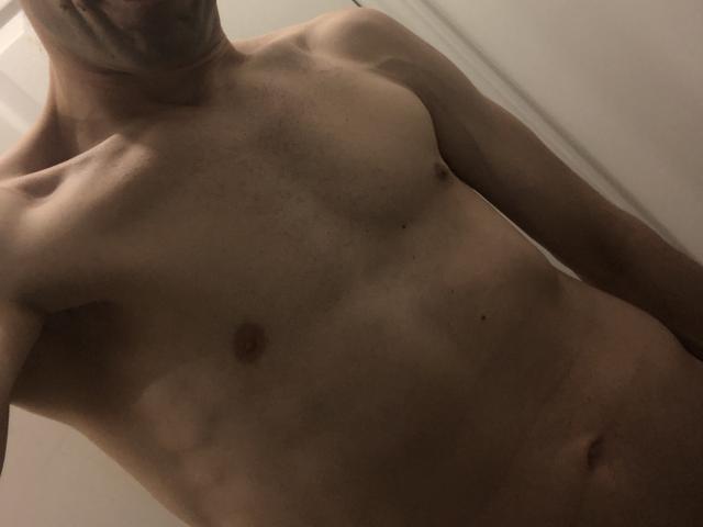 A topless ManalyEaters with a slim, toned body, visible nipples, and a faint tan line. His face is partially out of frame, with a shadowed neck.