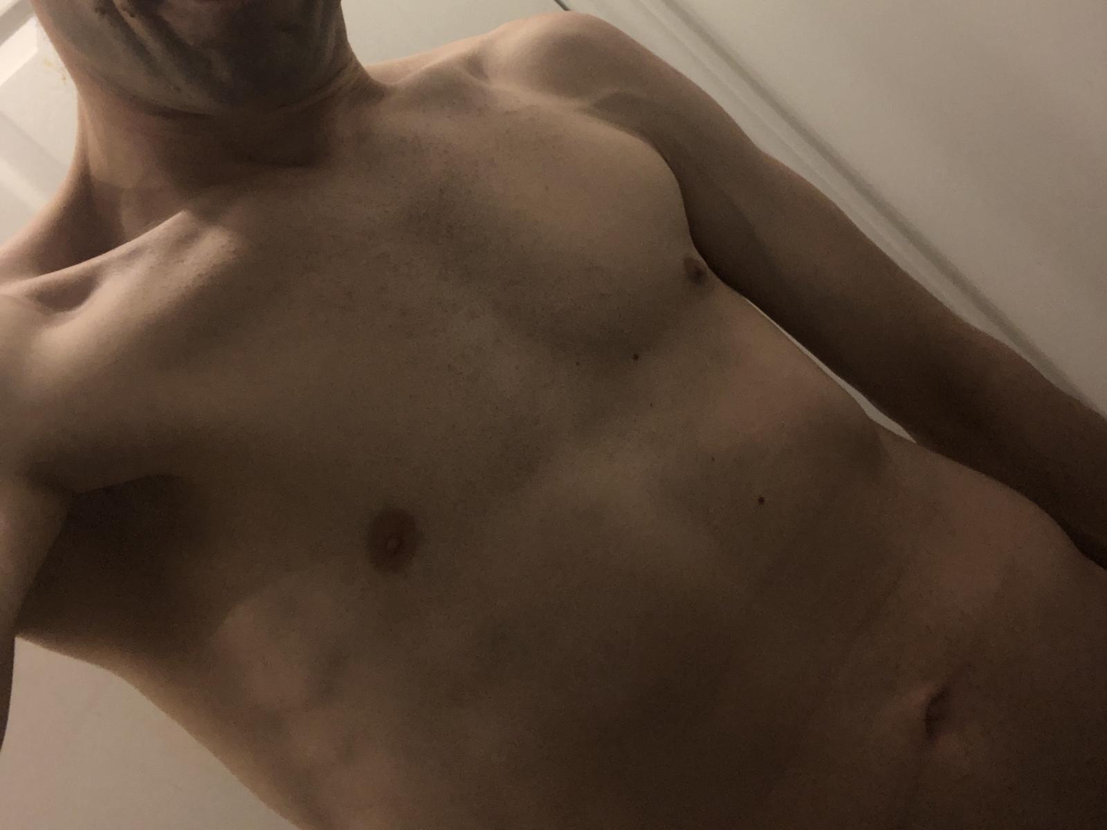 A topless ManalyEaters with a slim, toned body, visible nipples, and a faint tan line. His face is partially out of frame, with a shadowed neck.