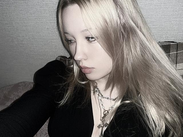 StarSice has long blonde hair, a black top, and a necklace with a heart and chain. She's looking down with a pouty face. Her tits are small.