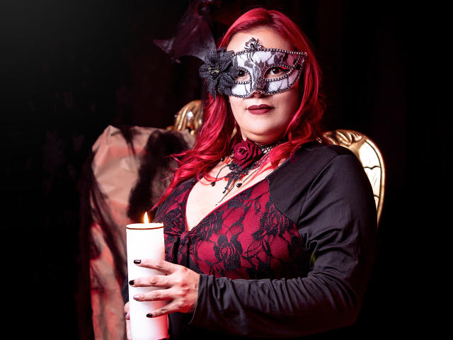 SammyOwens with red hair, black lace mask, red and black dress, holding white candle, looking at camera, dark background, flames on candle, visible tits, sexy, gothic vibe.