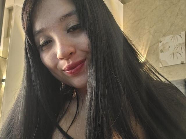 LunaBellaHotty has long black hair, light skin, and is smiling with red lips. She's wearing a black top, and her nose is slightly upturned. Her eyes are half-closed.