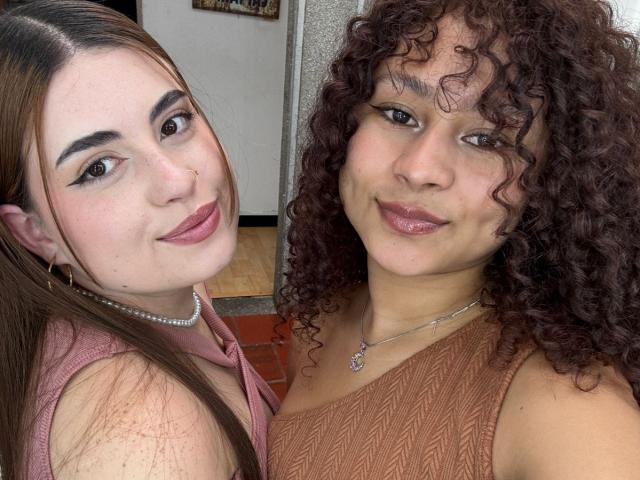 SofyViky with straight brown hair, pink lipstick, and pearl necklace, and SofyViky with curly brown hair, brown dress, and pink lipstick, smiling together. Both have cute faces.