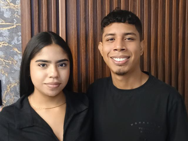 SofiAndLuis has dark brown skin, straight black hair, and small tits. Luis has a light brown skin, short curly black hair, and a visible ass. Both are smiling.