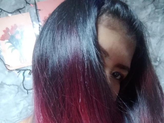 MariahSquirting69's dark, shiny hair with red ombre fades, covering her eyes. Her brown eyes are partially visible. Her skin is dark. Her eyebrows are thin.