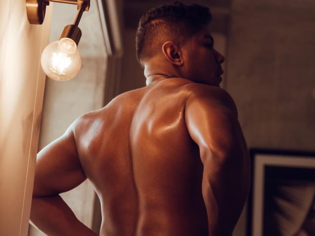 LeonHrz's sweaty, muscular back is glistening under a warm light, showing defined muscles and a short, buzzed haircut. His arms are slightly bent, looking over his shoulder.