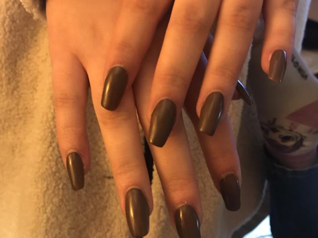 ElvinnaLaFrancaise's hands with long, shiny, dark brown, almond-shaped nails, resting on a soft, beige, textured surface. Her fingers are slightly spread, showcasing her manicure.