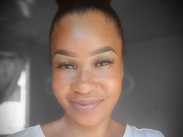 LeeBlaqX has a cute smile with light brown skin, brown eyes, and dark eyebrows, wearing nude eyeshadow, and has her hair in a high bun. She's looking directly at the camera.