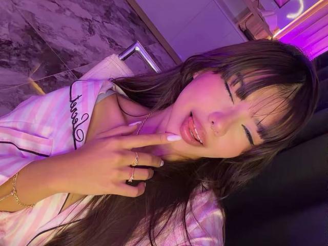 PrincessMiley with long brown hair, pink and white striped shirt, tongue out, eyes closed, and finger touching her lips, showing off her shiny pink nail and gold ring.