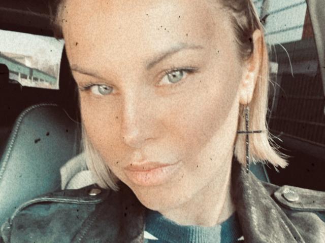 BelleLisaG's selfie showing her pouty lips, green eyes, and light blonde bob, wearing a leather jacket with earrings, sitting in a car.
