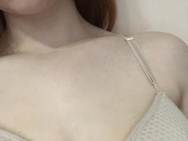 Auf einem Foto sind Pelerins blasse Haut, rotes Haar und kleine Brüste zu sehen. Sie trägt einen beige gefärbten, strukturierten BH mit dünnen Trägern. Ihr Schlüsselbein und der obere Teil ihrer Brust sind sichtbar..