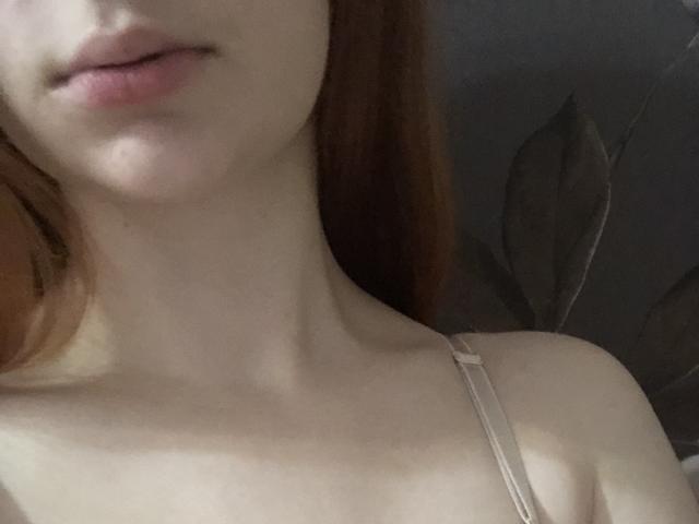 Pelerin hat eine blasse Haut, rotes Haar und rosafarbene Lippen. Ein sichtbarer Träger ist an ihrer Brust zu sehen, wodurch ihr zartes Schlüsselbein und ihr Oberkörper sichtbar werden. Brüste sind nicht sichtbar..