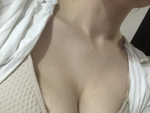 Pelerin's pale skin and cleavage are visible in a shot showing her collarbone and small, rounded boobs, dressed in a white shirt and beige, dotted top.