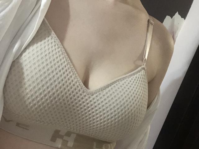 Pelerin's boobs in a beige, mesh-patterned bra with pink straps, slightly visible under a white shirt, showing some cleavage. Pelerin's skin is light.