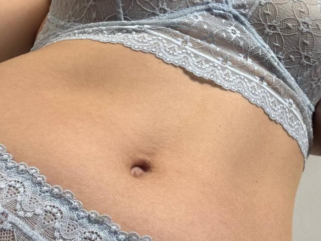 Close-up of MikyWayxy's midsection, showing a light tan, smooth, flat stomach with a small, round navel. MikyWayxy is wearing a lacey, light blue bra and matching lace panties, both with intricate floral patterns. The lace texture is detailed and delicate, contrasting with MikyWayxy's skin. The image focuses on the lower torso, highlighting the soft, natural curve and the subtle, even skin tone. The lace's semi-transparent quality adds a subtle, delicate visual element.