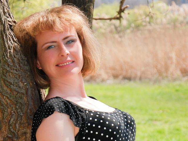 SunnySoul-hot with short red hair, blue eyes, and a cute smile, leaning against a tree in a black polka dot dress, showing her tits and ass slightly.