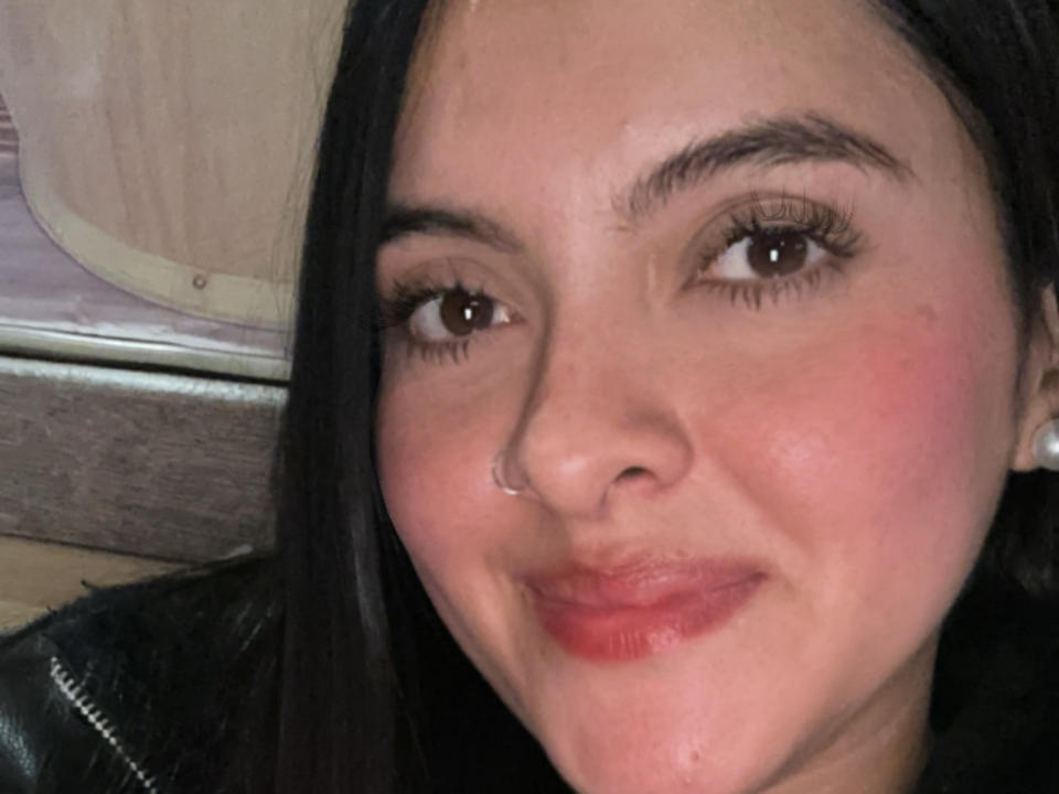 Mariaanm has a cute, smiling face with red lips, dark eyebrows, and long eyelashes. She's wearing a nose ring and has black hair, looking slightly flushed.
